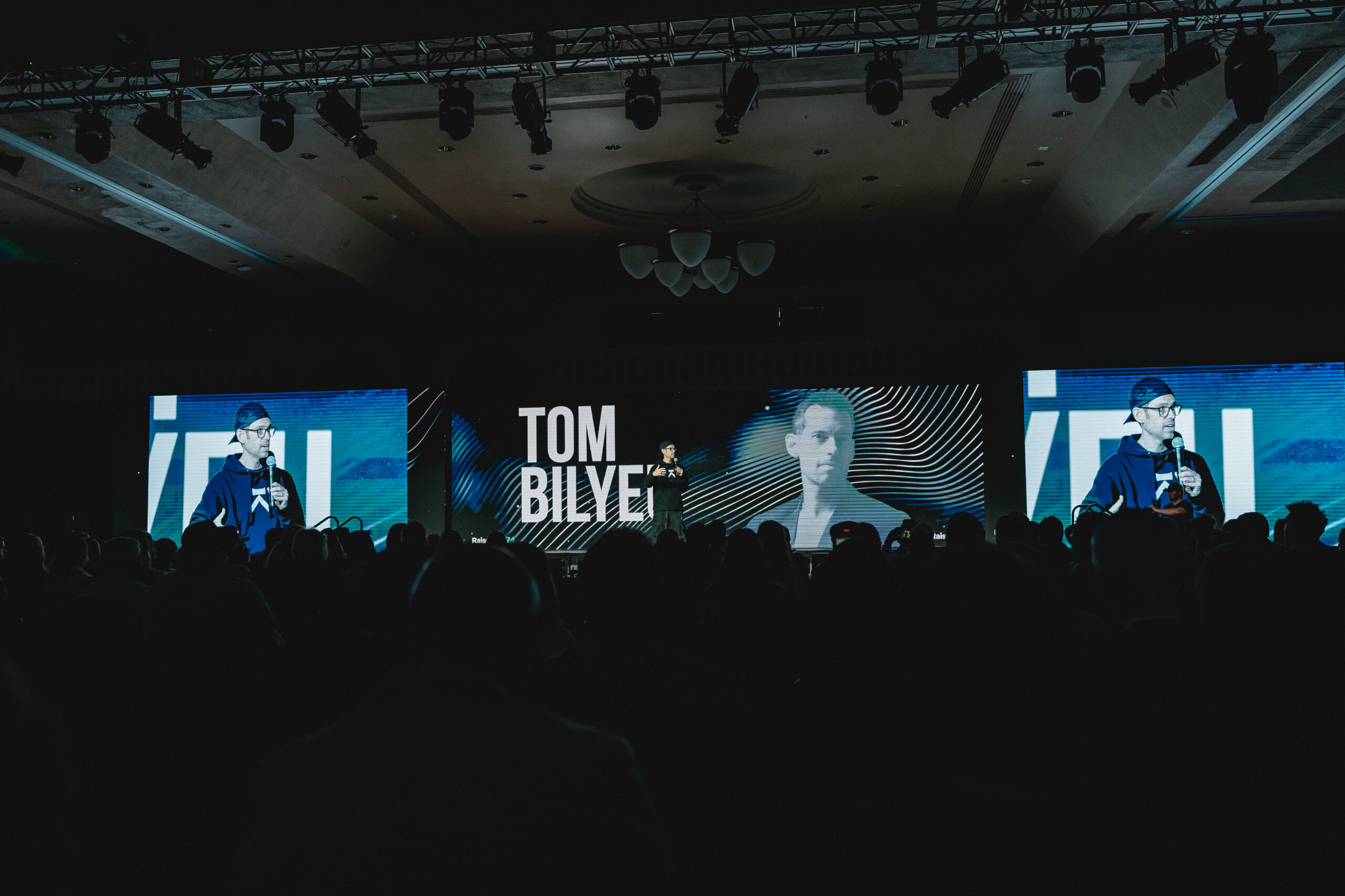 Tom Bilyeu delivering a speech on stage to a large crowd.